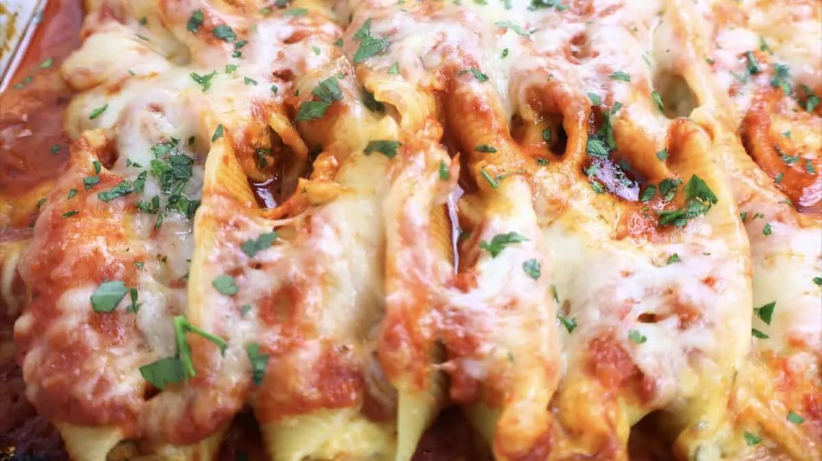 Close-up of baked stuffed pasta shells with melted cheese and fresh herbs in marinara sauce.